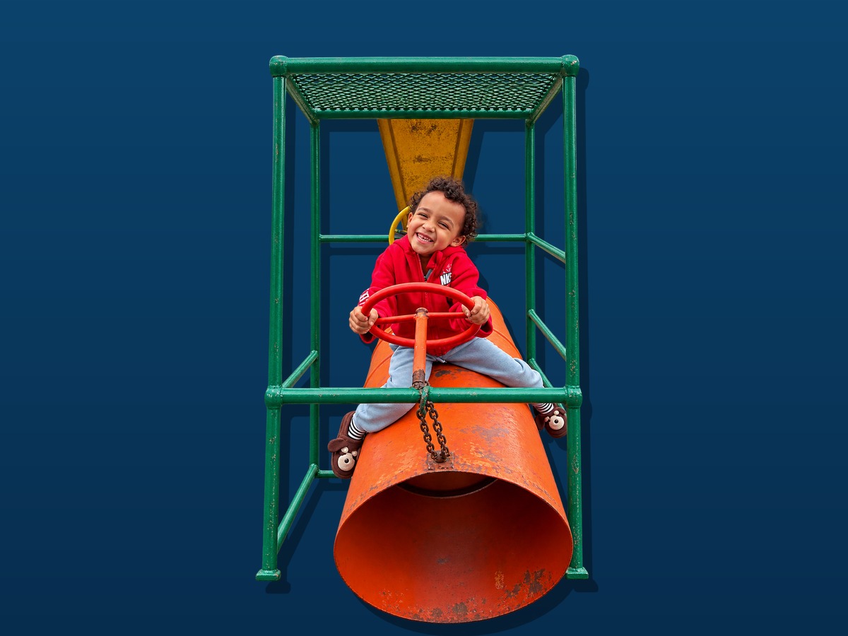 Young child smiling on a jungle gym during a Play-For-All activity